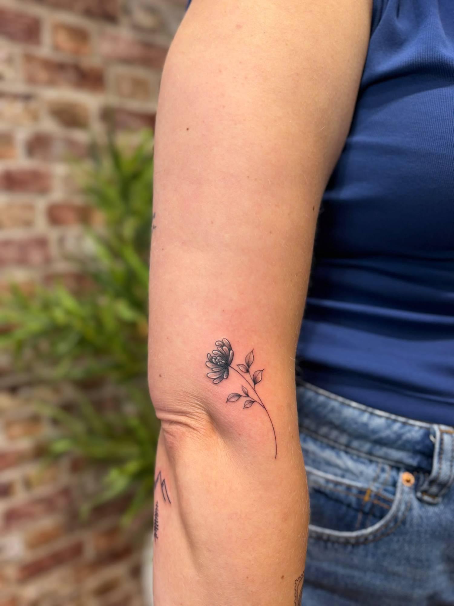 Delicate fine-line flower and leaves tattoo on an upper arm