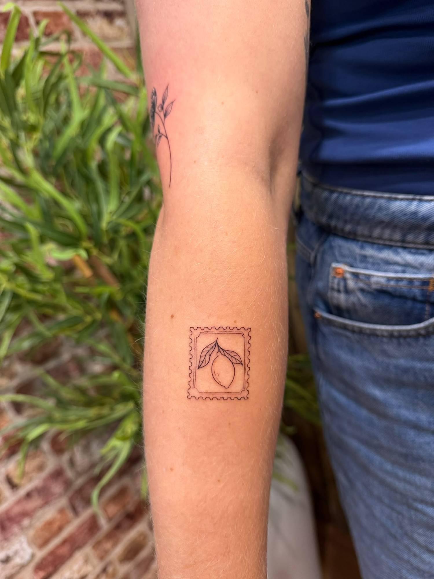 Fine-line postage stamp tattoo of a lemon on a forearm